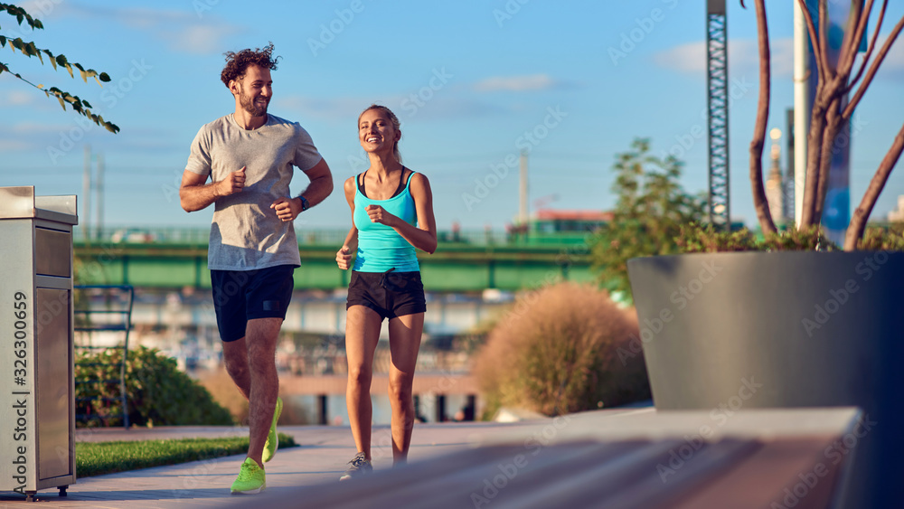 Modern woman and man jogging / exercising in urban surroundings near the river. - obrazy, fototapety, plakaty 