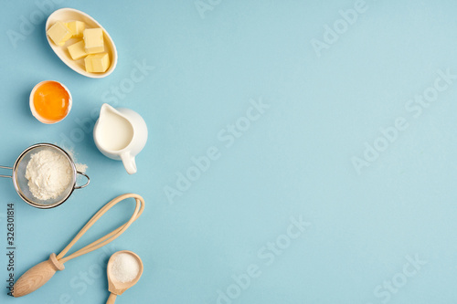 Baking background with whisk, egg, flour , sugar, butter on blue table top view. Flat lay.