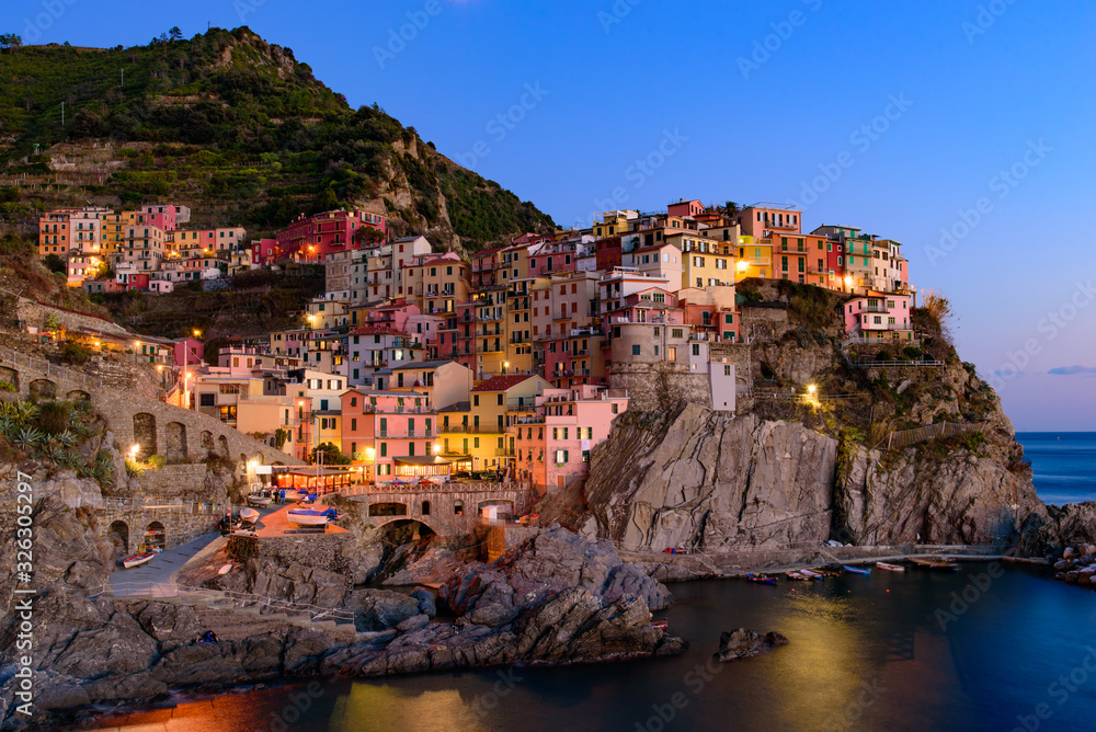 Sunset and night view of Manarola, one of the five Mediterranean villages in Cinque Terre, Italy, famous for its colorful houses and harbor