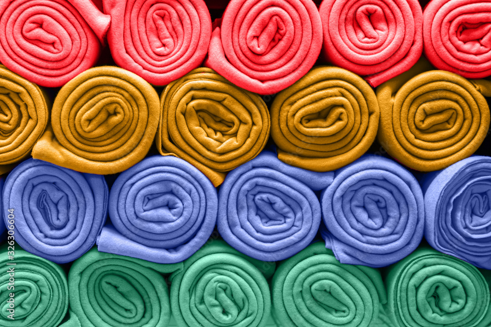 A bunch of colorful blankets folded in rows. Rolls of colored rugs lie on a shelf, texture effect. A bunch of colorful blankets folded in rows. Rolls of colored rugs lie on a shelf, texture effect.