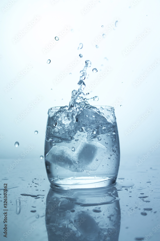 Ice falling glass of water, a splash of ice cube with splashes, pure drinking water in a transparent glass Ice falling glass of water, a splash of ice cube with splashes, pure drinking water in a transparent glass