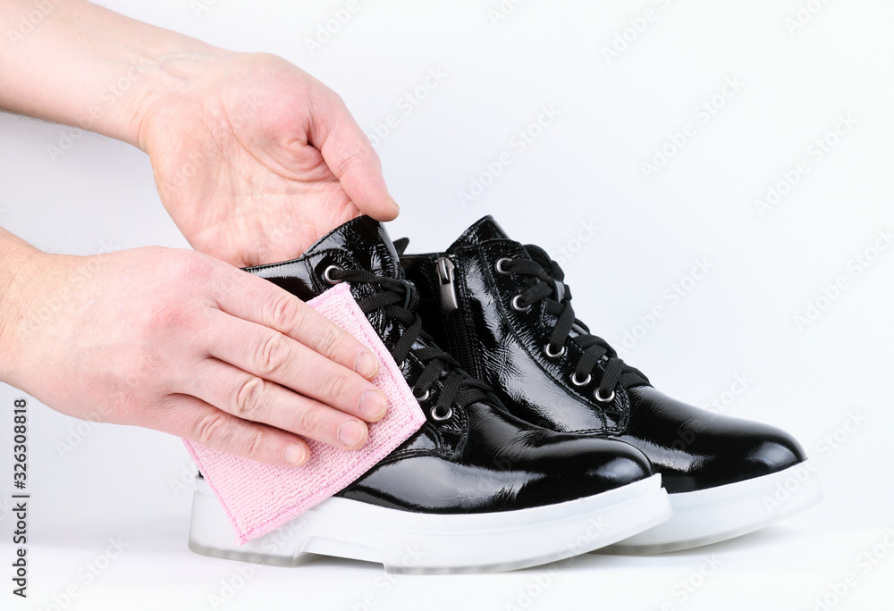Man's hands wipe a patent leather boot from dirt dust on a white background. Care for patent leather shoes.Protection of shoes in rainy, wet weather.