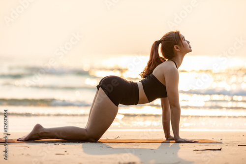 Vacation of Asian woman relaxing in yoga Cat pose on sand and beach with sunset sea in Thailand Tropical island,Feel comfortable and relax in holiday photo