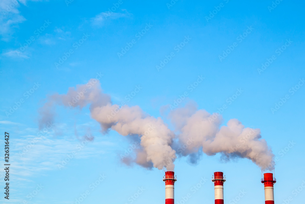 Smoking industrial stacks in a thermal power plant emit polluted air into the atmosphere in the blue sky - obrazy, fototapety, plakaty 