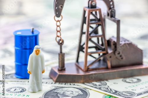 Crude oil price and petroleum demand concept :  Arab men in white thawbs negotiate on a trade deal or buying contract. Oil rig or pumpjack and black crude oil drum barrels on US USD dollar banknotes. photo