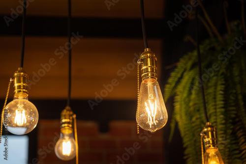 Fotografia Electrical classic light bulb in warm light color which is hanging down from the ceiling, using as interior decorative for retro and vintage style