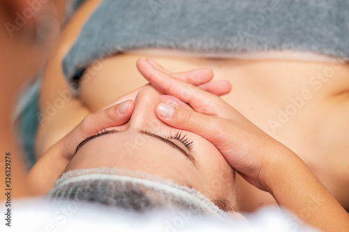Beautiful young woman receiving face massage at beauty salon  close up.