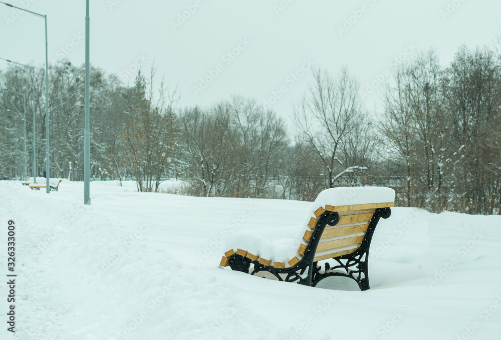 Benches standing in the winter time in the city Park in the daytime littered with a large amount of snow