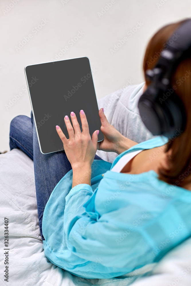 Obraz premium people, technology and leisure concept - young woman sitting on sofa with tablet pc computer and headphones listening to music at home
