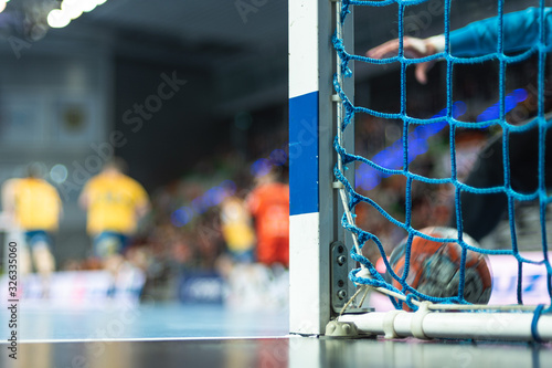 Detail of handball goal post with net and handball match in the background.