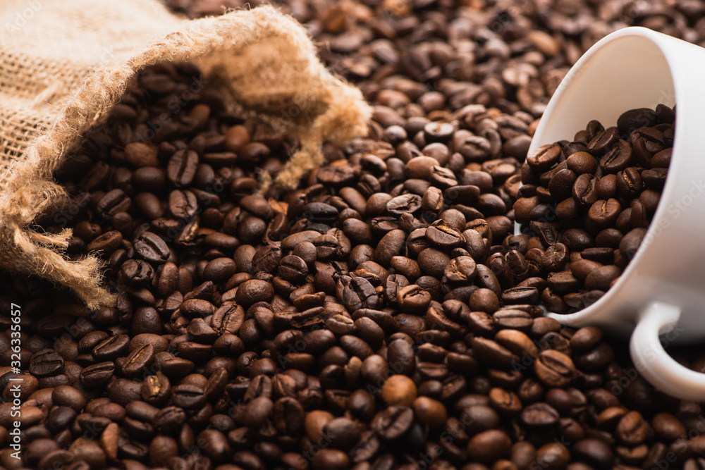 Fototapeta premium selective focus of fresh roasted coffee beans and white cup near sack