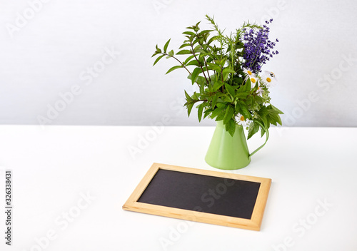 gardening, plants and organic concept - bunch of herbs and flowers in green jug with chalkboard on table