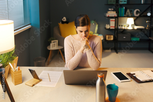 Fotografija Young woman sitting at desk and using her laptop