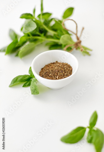 greens  culinary and flavoring concept - bunch of fresh basil herb and dry seasoning in cup on white background