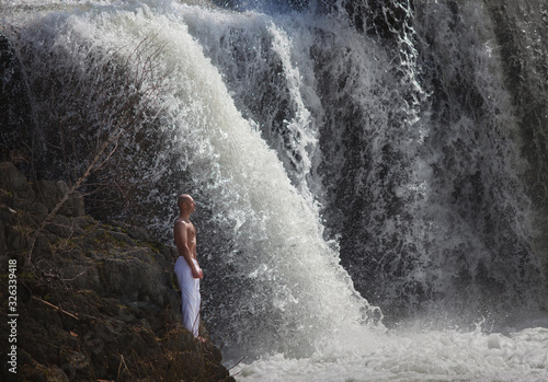 Buddhist. Bald man. Meditation in the mountains against the backdrop of a waterfall. Prayer.