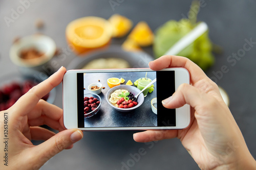 food, eating and breakfast concept - hand of woman taking picture of cereals in bowl with fruits, berries and juice with smartphone