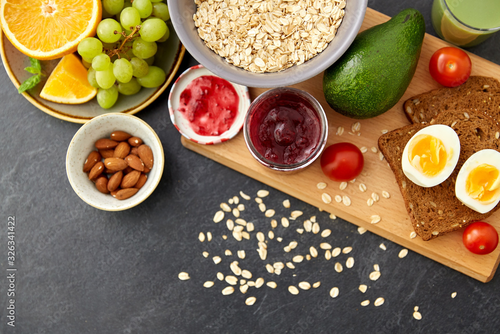 food, eating and breakfast concept - oatmeal cereals in bowl, fruits, almond nuts, jam and toast bread on slate stone table food, eating and breakfast concept - oatmeal cereals in bowl, fruits, almond nuts, jam and toast bread on slate stone table