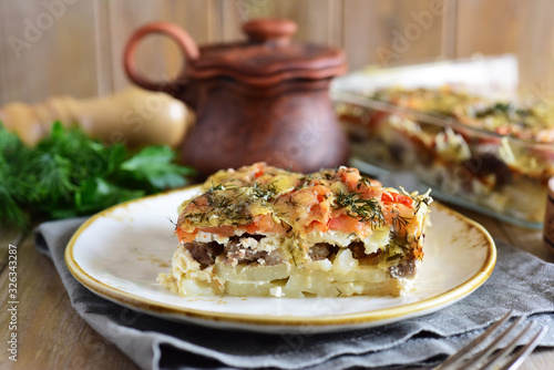Delicious meat casserole with vegetables on a white plate close up on a wooden table