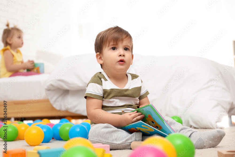Cute little boy with book playing on floor while girl sitting on bed. Children's development Cute little boy with book playing on floor while girl sitting on bed. Children's development