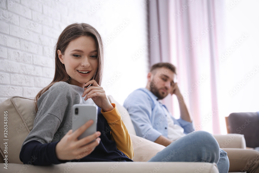 Young man peering into girlfriend's smartphone at home, focus on woman. Relationship problems Young man peering into girlfriend's smartphone at home, focus on woman. Relationship problems