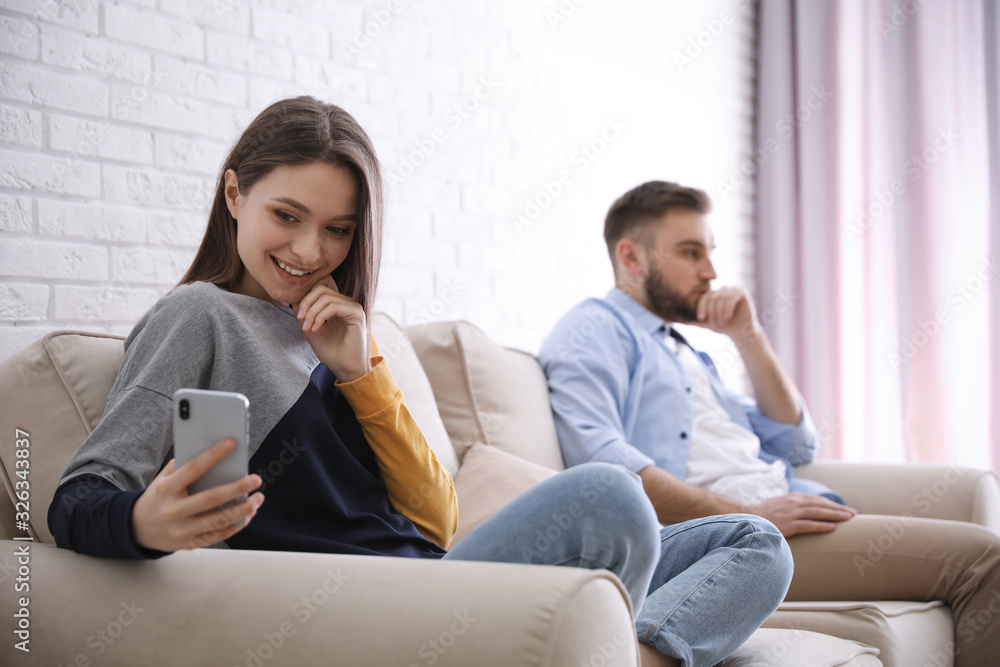 Young woman with smartphone ignoring her boyfriend at home. Relationship problems Young woman with smartphone ignoring her boyfriend at home. Relationship problems