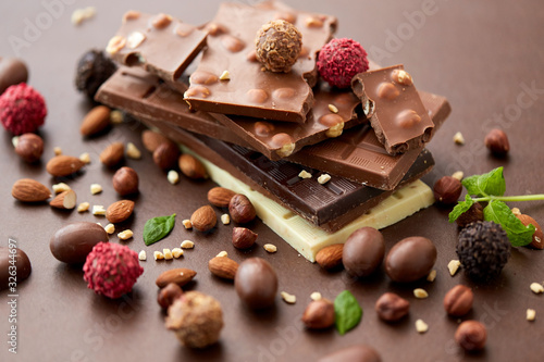 sweets, confectionery and food concept - close up of different chocolate bars, candies and nuts on brown background