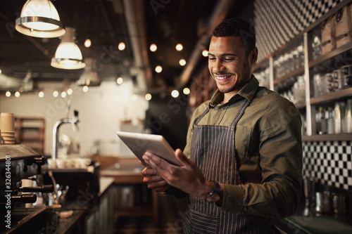 Portrait of successful young afro-american cafe owner standing behind counter using digital tablet