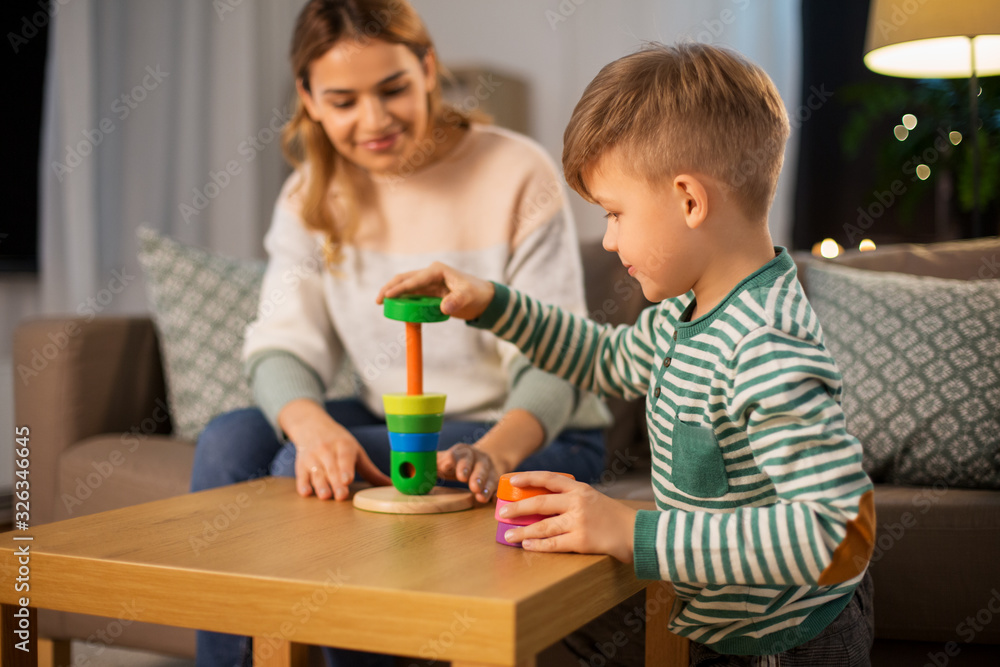 family, leisure and people concept - happy smiling mother and son playing with toy pyramid at home in evening family, leisure and people concept - happy smiling mother and son playing with toy pyramid at home in evening