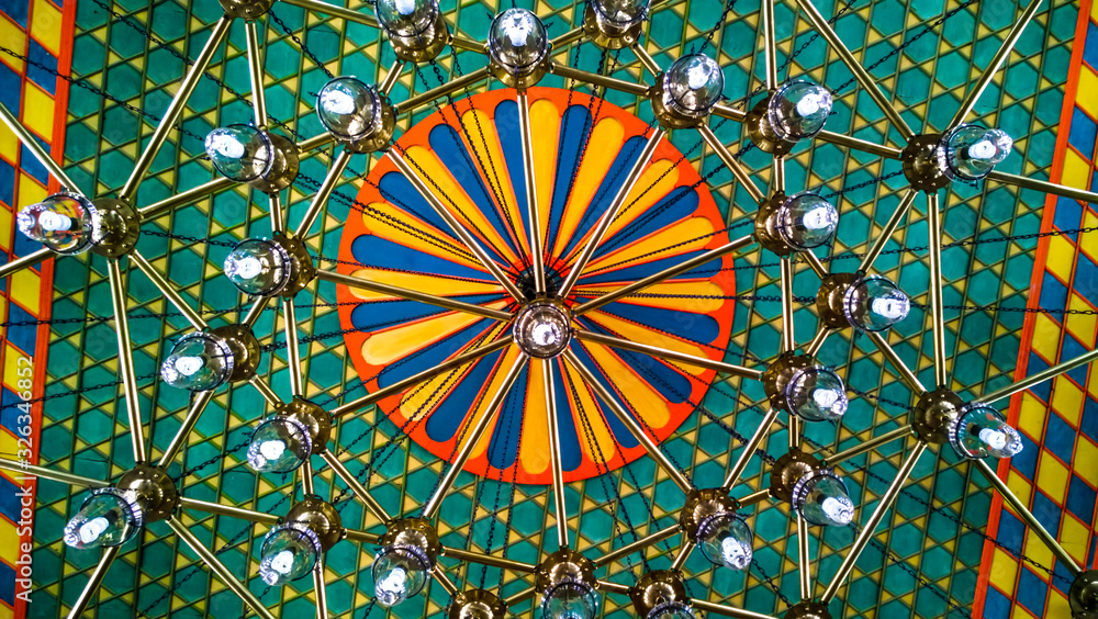 Oriental ceiling in different colors with colorful ornaments in green colors and large chandelier hanging, an interesting eastern design of the building interior