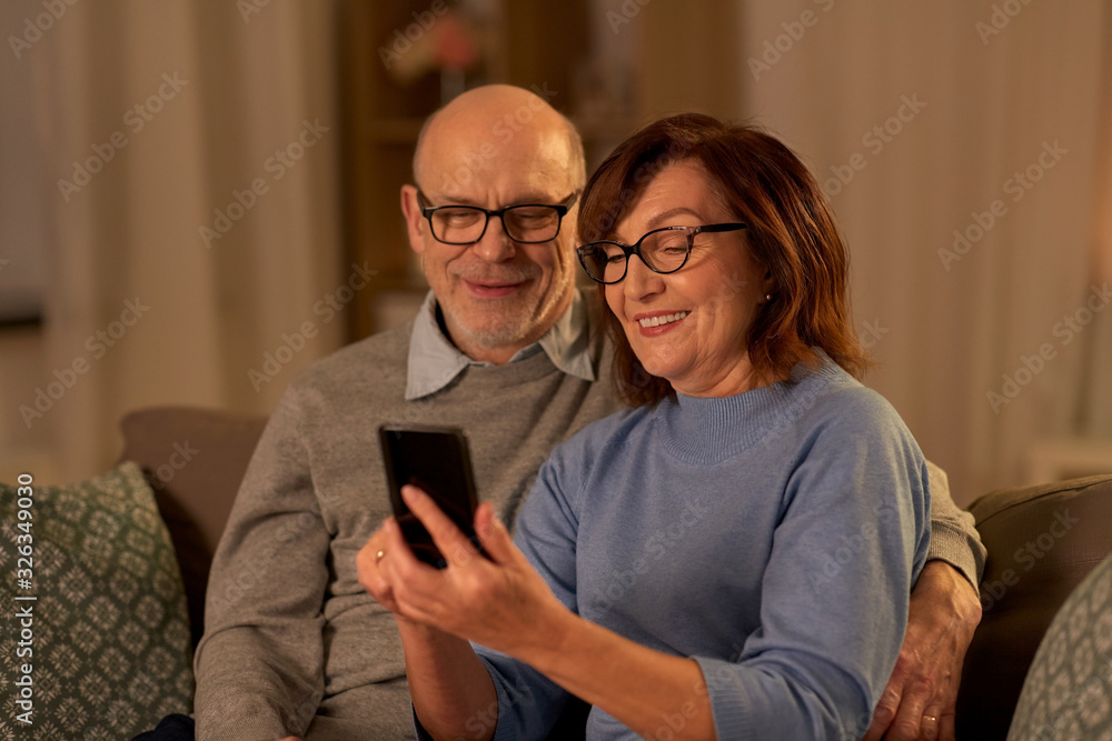 technology, old age and people concept - happy senior couple with smartphone at home in evening technology, old age and people concept - happy senior couple with smartphone at home in evening