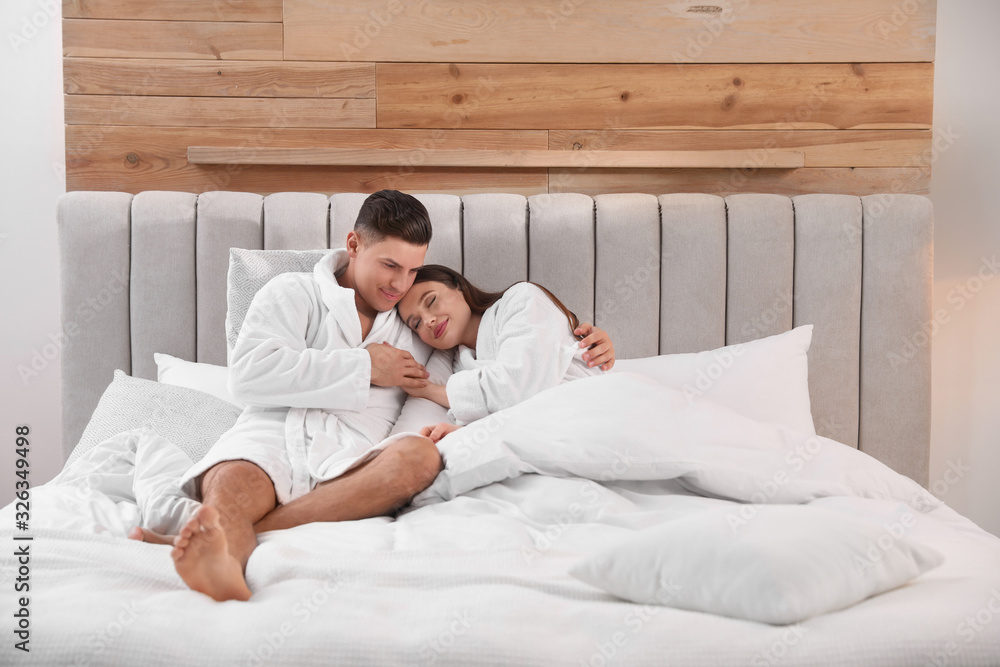 Fototapeta premium Happy couple in bathrobes resting on bed at home