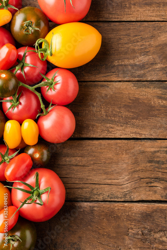 Different tomatoes on rustic wooden background with copyspace. Top view