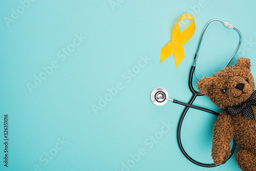 Top view of yellow ribbon, toy and stethoscope on blue background, international childhood cancer day concept photo