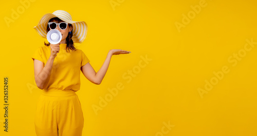 Cute and funny woman in yellow casual cloth style and wearing hat holding white megaphone for announcement and show hand to present product.