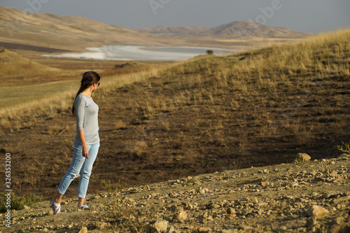 Young woman with long hair standing elegant in the middle of desert field on background of mountains, view from side