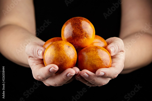 Blood oranges with red peel in hands on black background