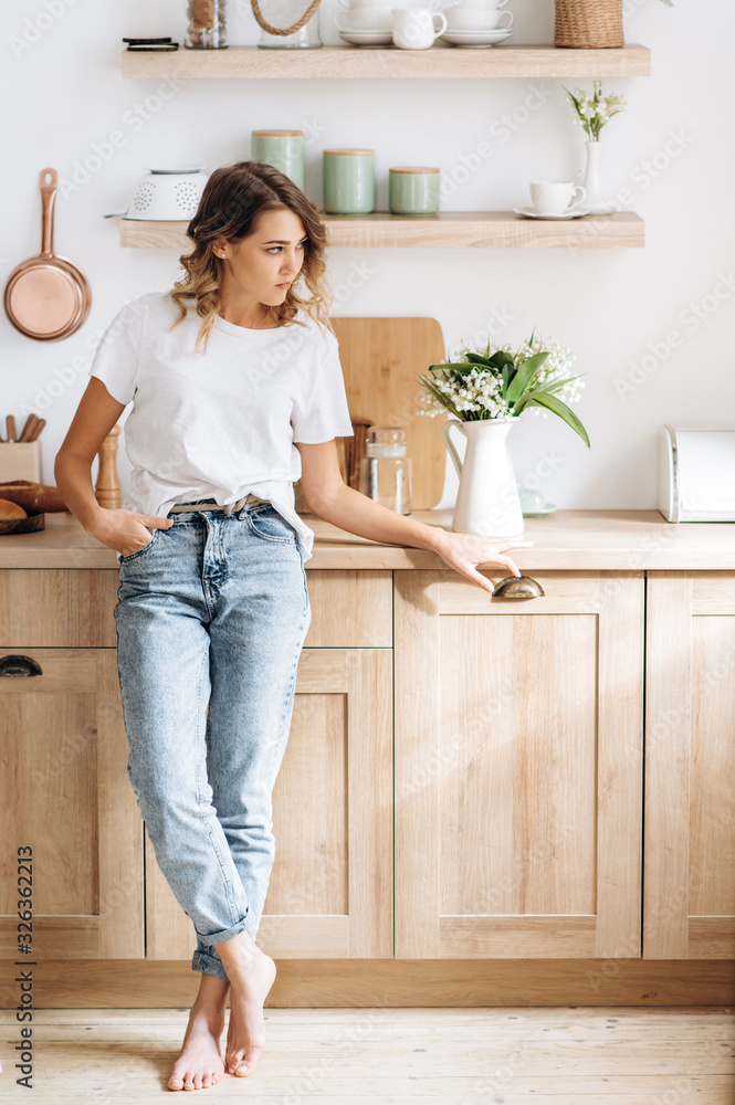Portrait of an amazing young blue-eyed blonde girl in a stylish casual clothes. She is posing beautifully in the kitchen Portrait of an amazing young blue-eyed blonde girl in a stylish casual clothes. She is posing beautifully in the kitchen