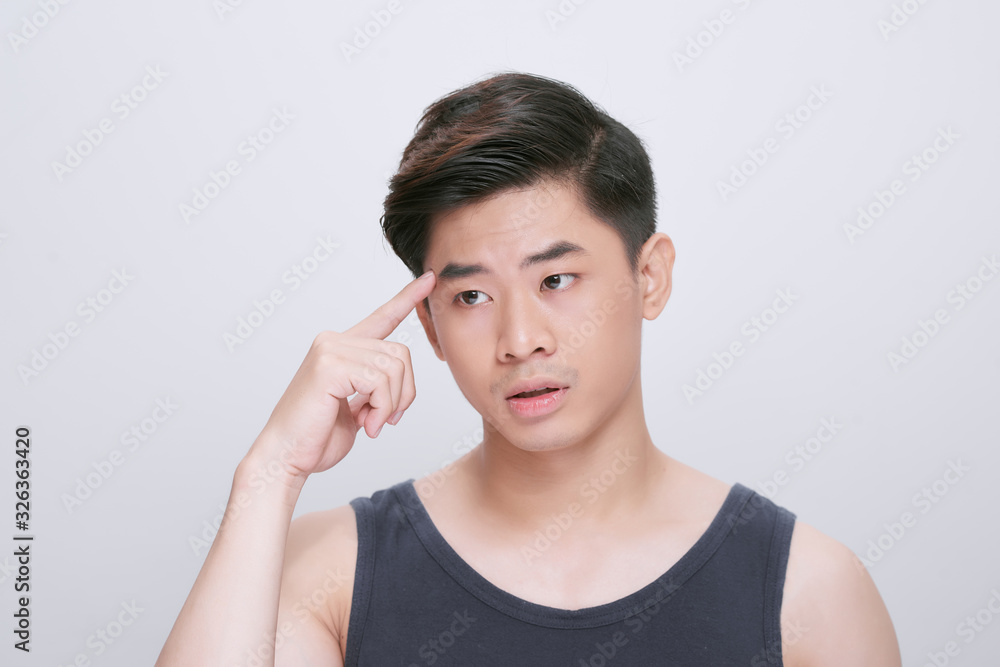Young asian chinese man wearing t-shirt standing over isolated white background pointing unhappy to pimple on forehead, ugly infection of blackhead. Acne and skin problem Young asian chinese man wearing t-shirt standing over isolated white background pointing unhappy to pimple on forehead, ugly infection of blackhead. Acne and skin problem