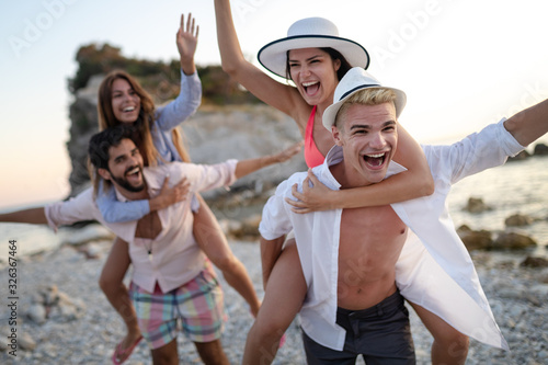 Group of friends having fun on the beach under sunset on vacation