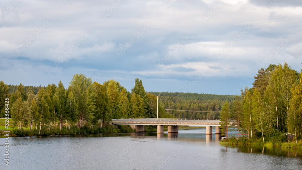 Bridge over the pond. A fabulous landscape of a Finnish lake in the midst of a dense Scandinavian green forest. The concept of calm and quiet rest in the most environmentally friendly country. Bridge over the pond. A fabulous landscape of a Finnish lake in the midst of a dense Scandinavian green forest. The concept of calm and quiet rest in the most environmentally friendly country.