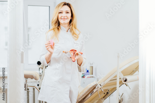 Doctor gynecologist holding anatomical model of uterus and menstrual cup, talking about intimate hygiene menstrual eco cup, how use, to female patient in an chair in modern medical office. photo