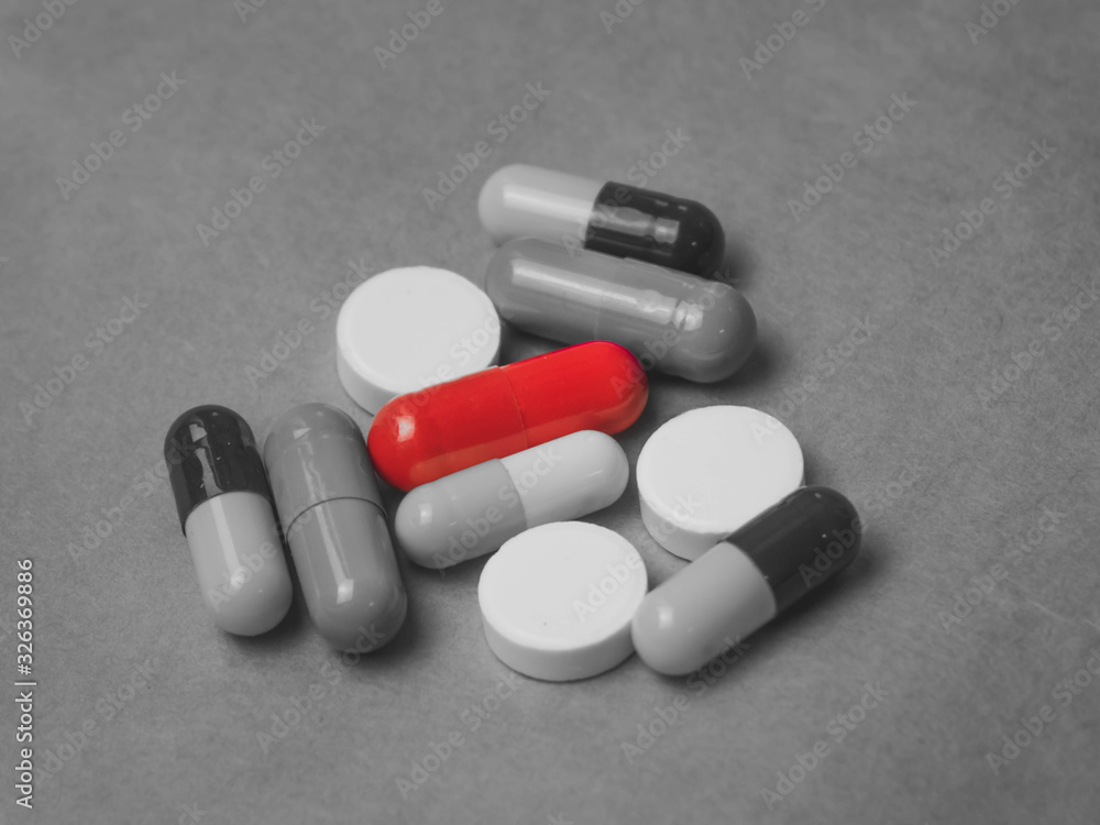 black and white photo with tablets and one capsule among them red color black and white photo with tablets and one capsule among them red color