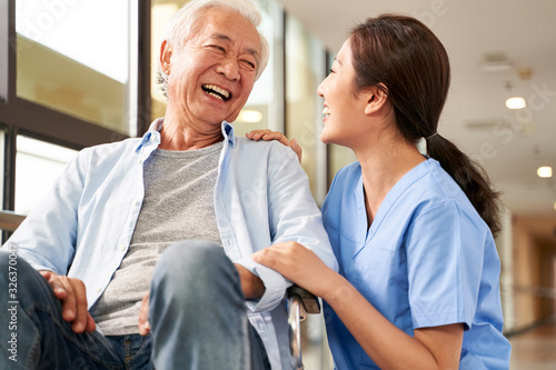 young friendly asian female caregiver talking to elderly man in nursing home photo