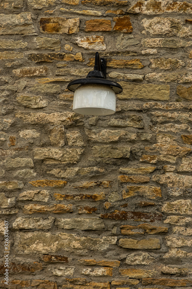 Alte gepflegte Stadtmauer aus Naturstein mit sehr flachen und breiten Steinen von gelblich hell bis  rostbraun mit schöner Vintage Außenleuchte aus Glas und schwarzem Metallschirm mit Haltearm