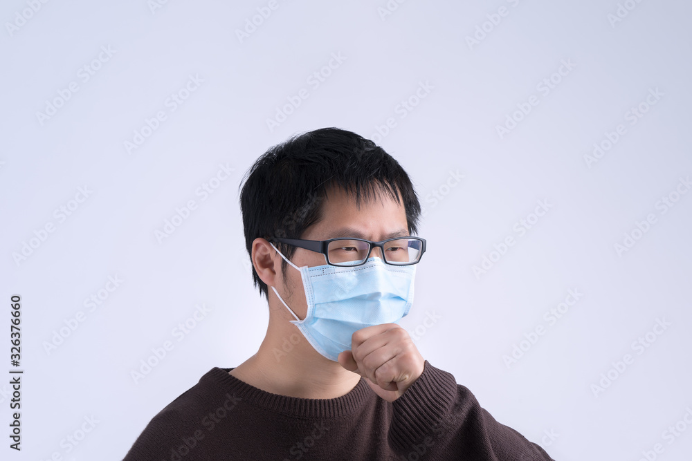 Young Asian man is coughing, feeling unwell, vomit sick with wearing a medical blue face mask isolated on white background, close up, copy space. Young Asian man is coughing, feeling unwell, vomit sick with wearing a medical blue face mask isolated on white background, close up, copy space.