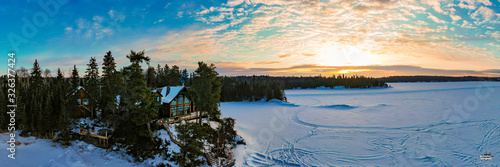 A snowy winter cabin overlooking a frozen lake during a beautiful bright sunrise.