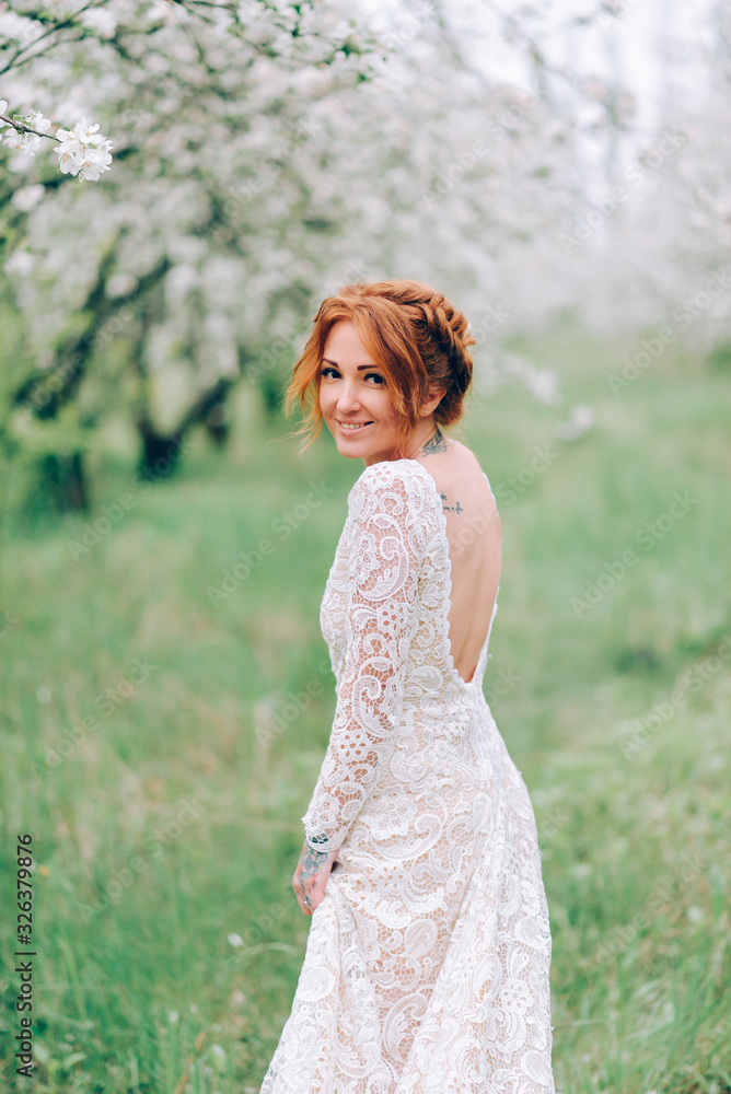 Young beautiful woman in a white dress is standing in a blooming garden.