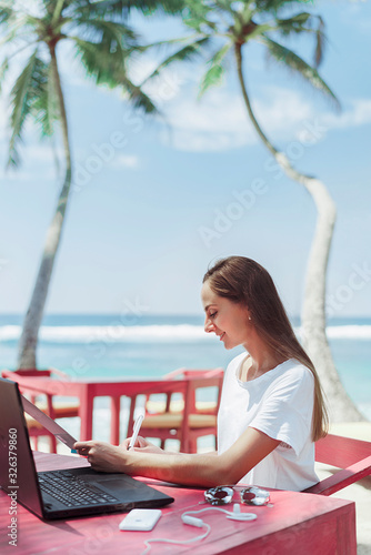 Woman freelancer on the ocean in the tropics working at the pink table
