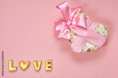 Heart shaped Valentines Day gift box with pink curved ribbon and gold word love on paper background. Top view, flat lay. © wertinio