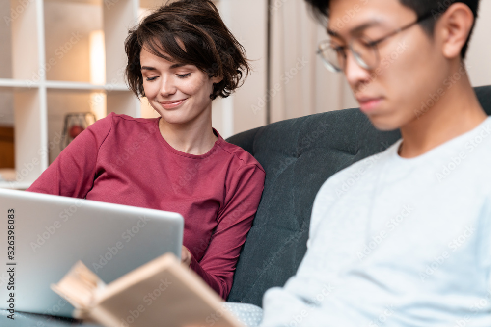 Photo of pleased multinational couple reading book and using laptop Photo of pleased multinational couple reading book and using laptop